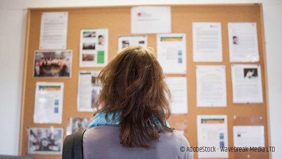 Frau steht vor Aushängen und liest