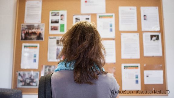 Frau steht vor einer Wandzeitung und liest Aushänge